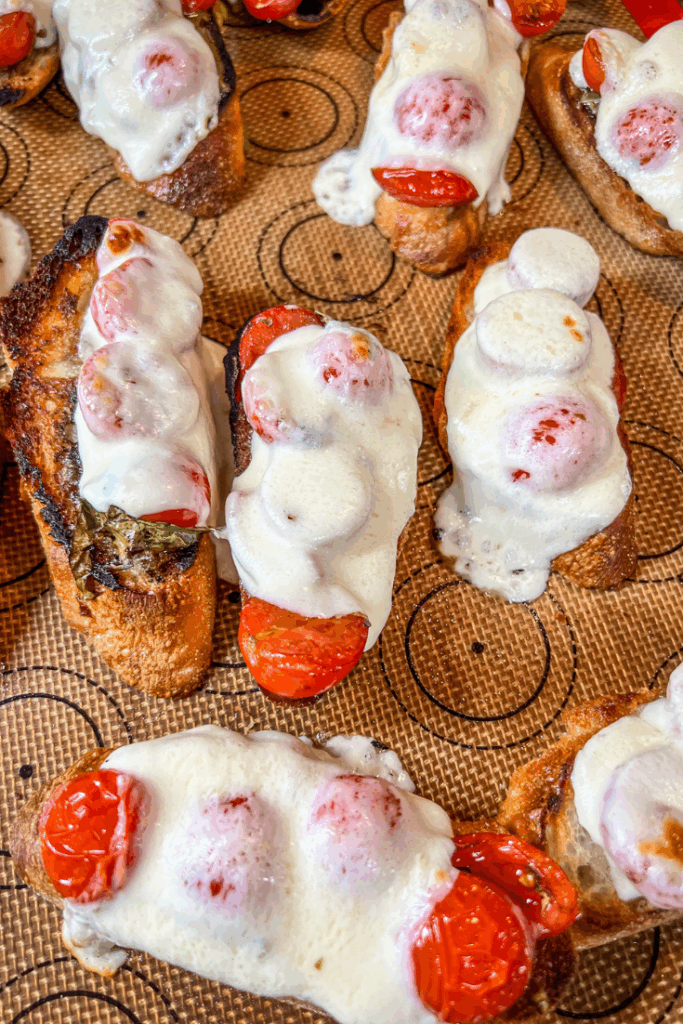 crostini topped with cheese and tomatoes on a baking sheet
