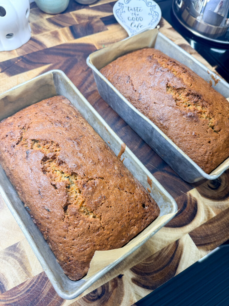 Two golden brown baked zucchini loaves cooling on a wooden cutting board after being released from pans