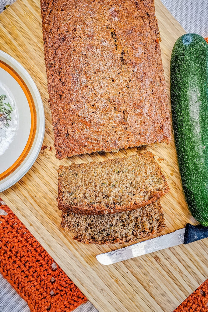 Two sliced zucchini bread loaves on a wooden board showing tender golden interior with green zucchini visible