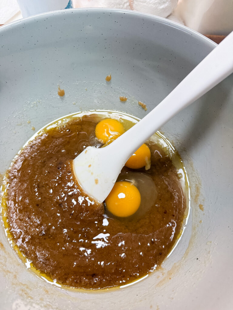 Speckled mixing bowl with wet ingredients and three beaten eggs being added to the brown butter and sugar mixture