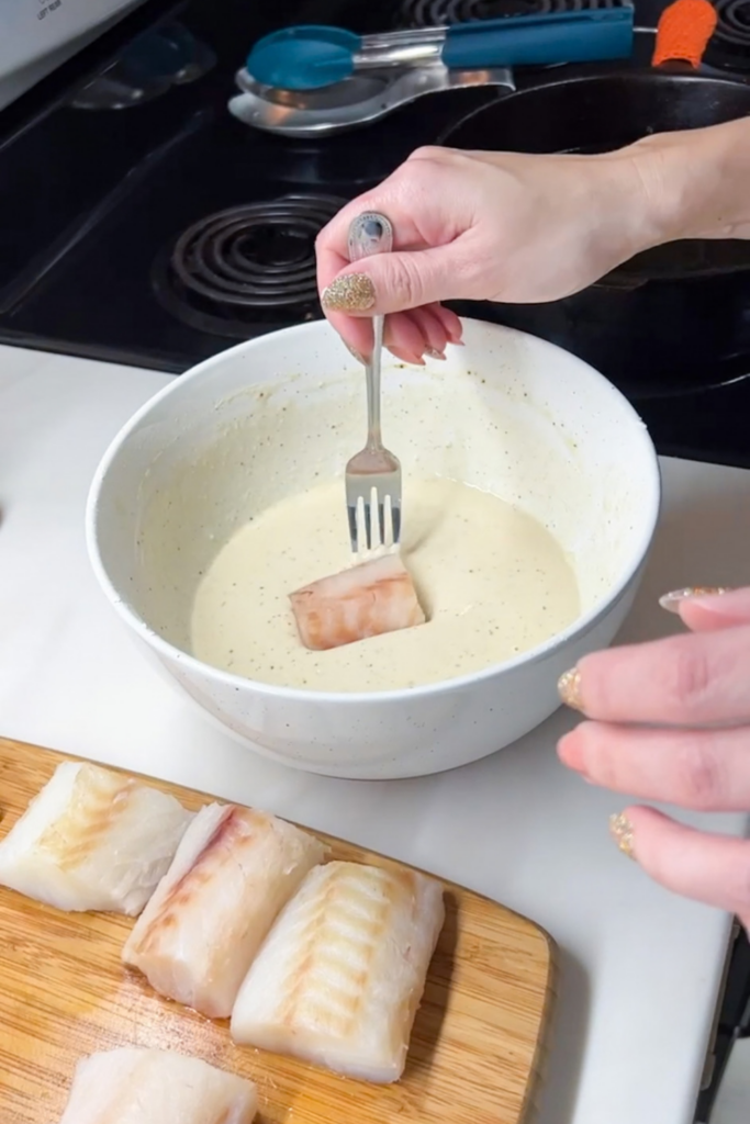 Fish piece being dipped into thick beer batter before frying