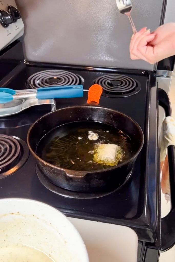 Beer battered fish frying in hot oil in cast iron pan