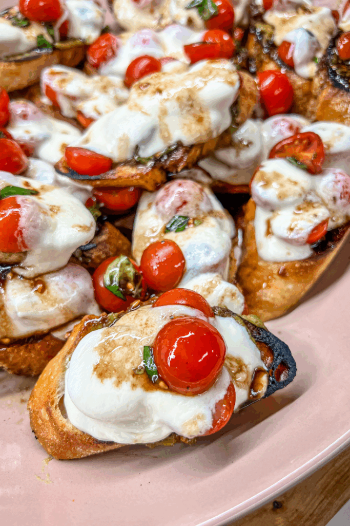 roasted tomato avocado and mozzarella crostini on a pink platter