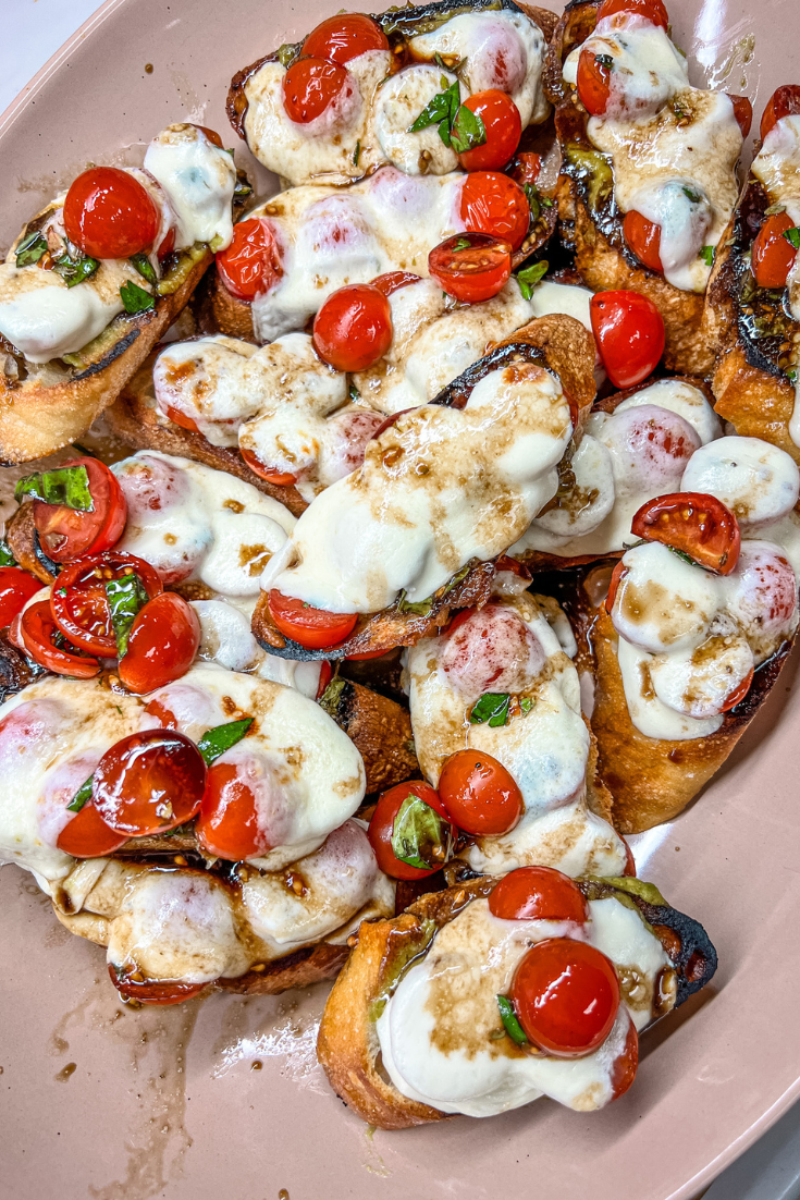 roasted tomato, avocado, and mozzarella crostini on a pink platter
