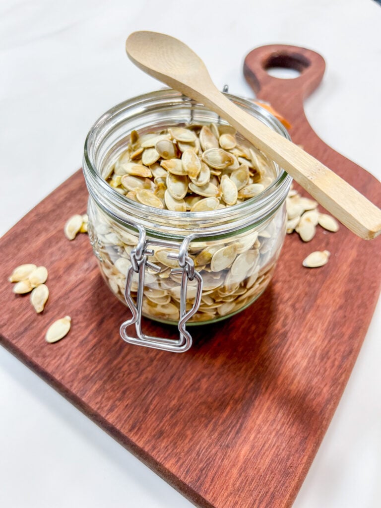 Jar of homemade roasted pumpkin seeds on a wooden cutting board