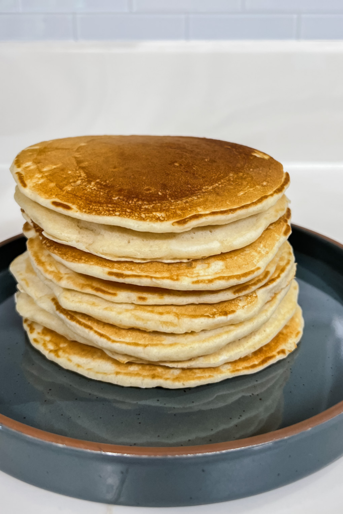 Pancakes that were cooked on the griddle stacked on a ceramic plate.