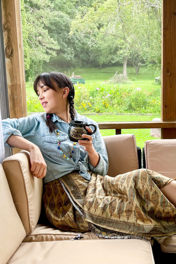 a person sitting on a couch holding a cup of coffee wearing a jean button top and brown skirt