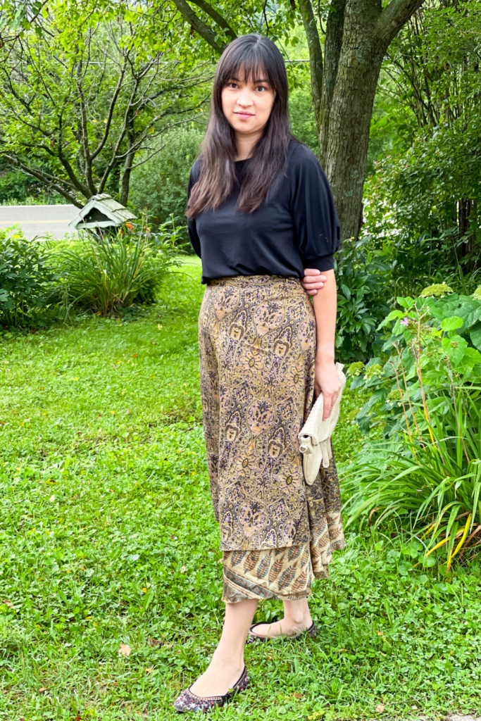 an individual wearing a black top and brown skirt holding a cream envelope clutch