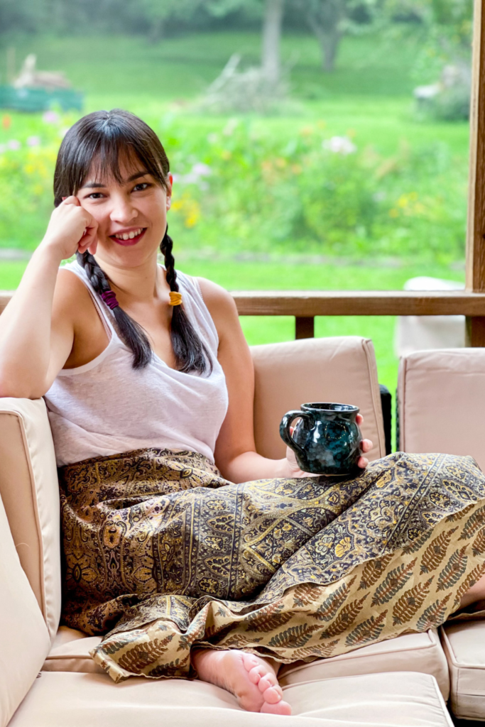 a person sitting on a couch wearing a white linen tank top and brown skirt