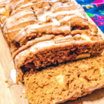 Finished Apple pumpkin Bread with glaze. Sitting on a Cutting board sliced to show the apple chucnks.