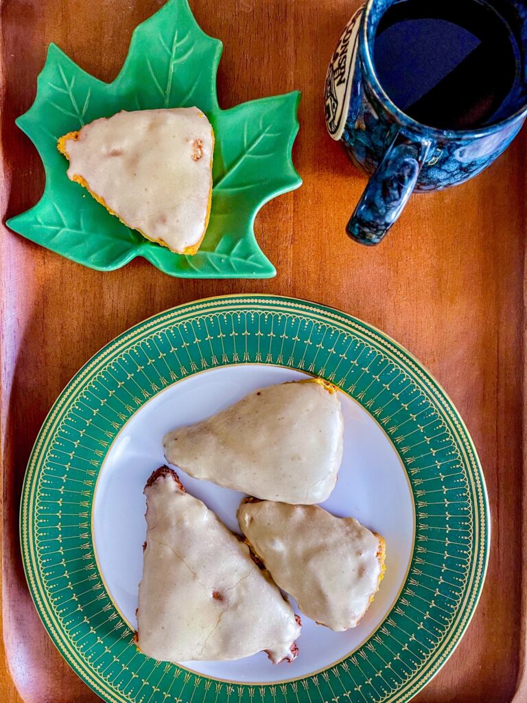 Pumpkin scones oln a plate next to a cup of coffee on a wood tray