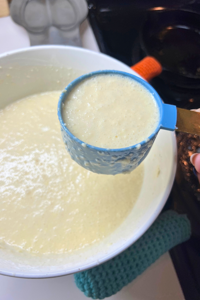 a person holding a measuring spoon over a bowl of batter