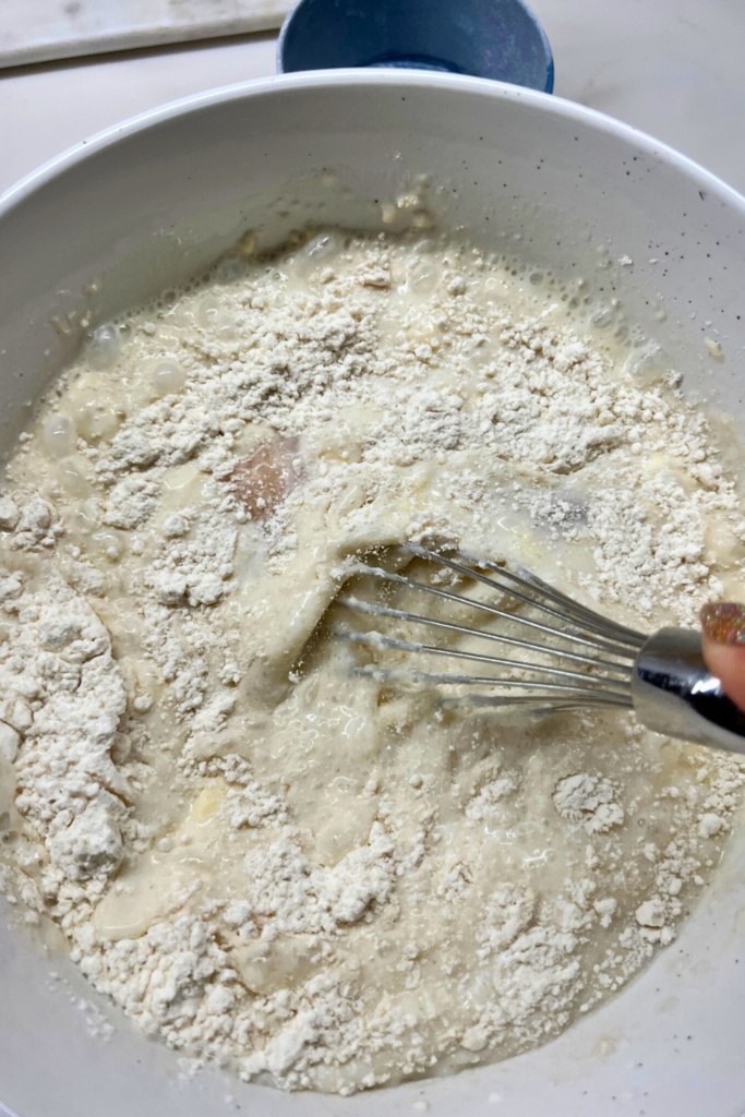 a person holding a whisk in a bowl of diner pancake ingredients