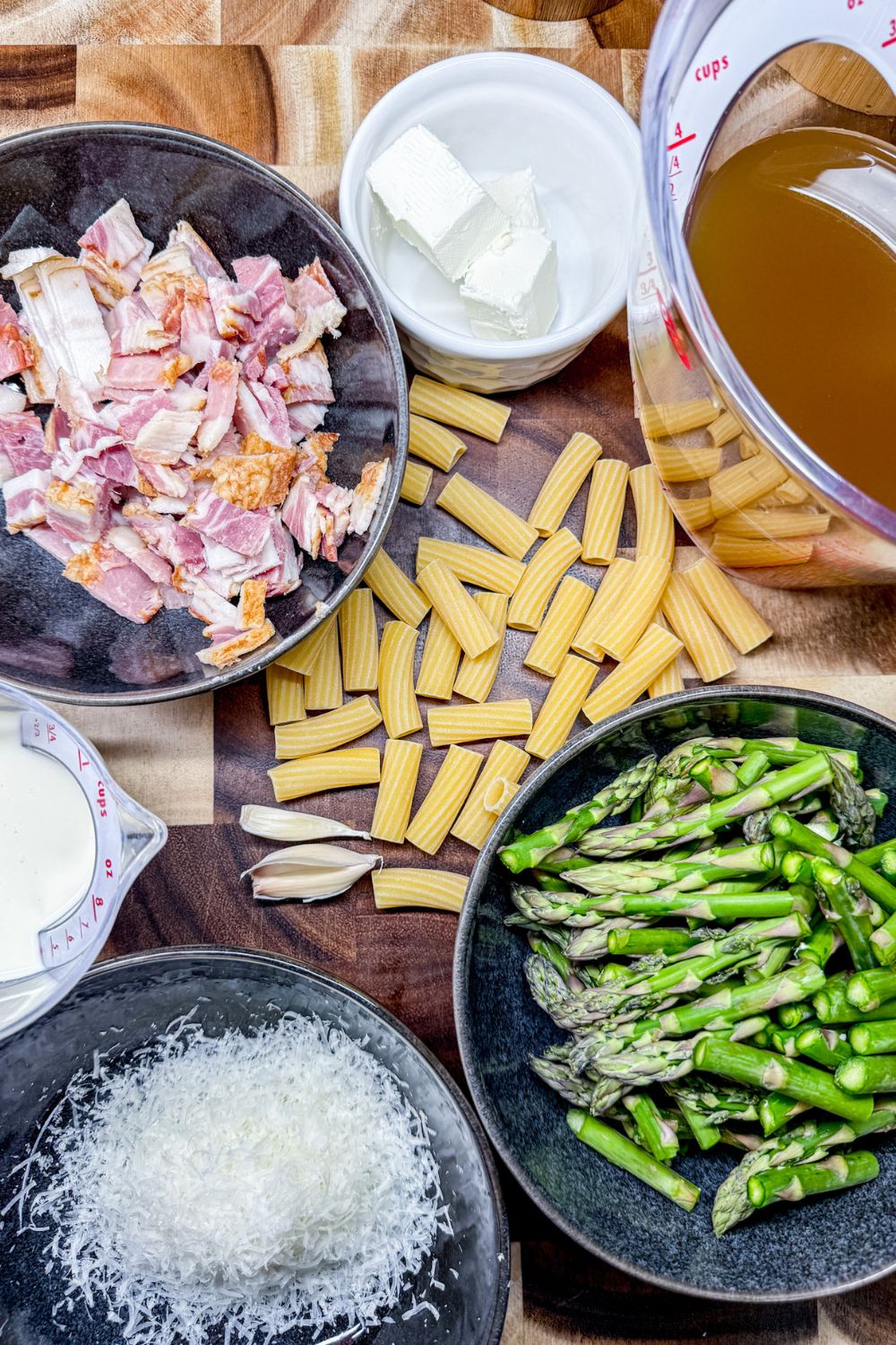 Ingredients for one pot asparagus and bacon rigatoni including bacon, pasta, asparagus, broth, and cheese