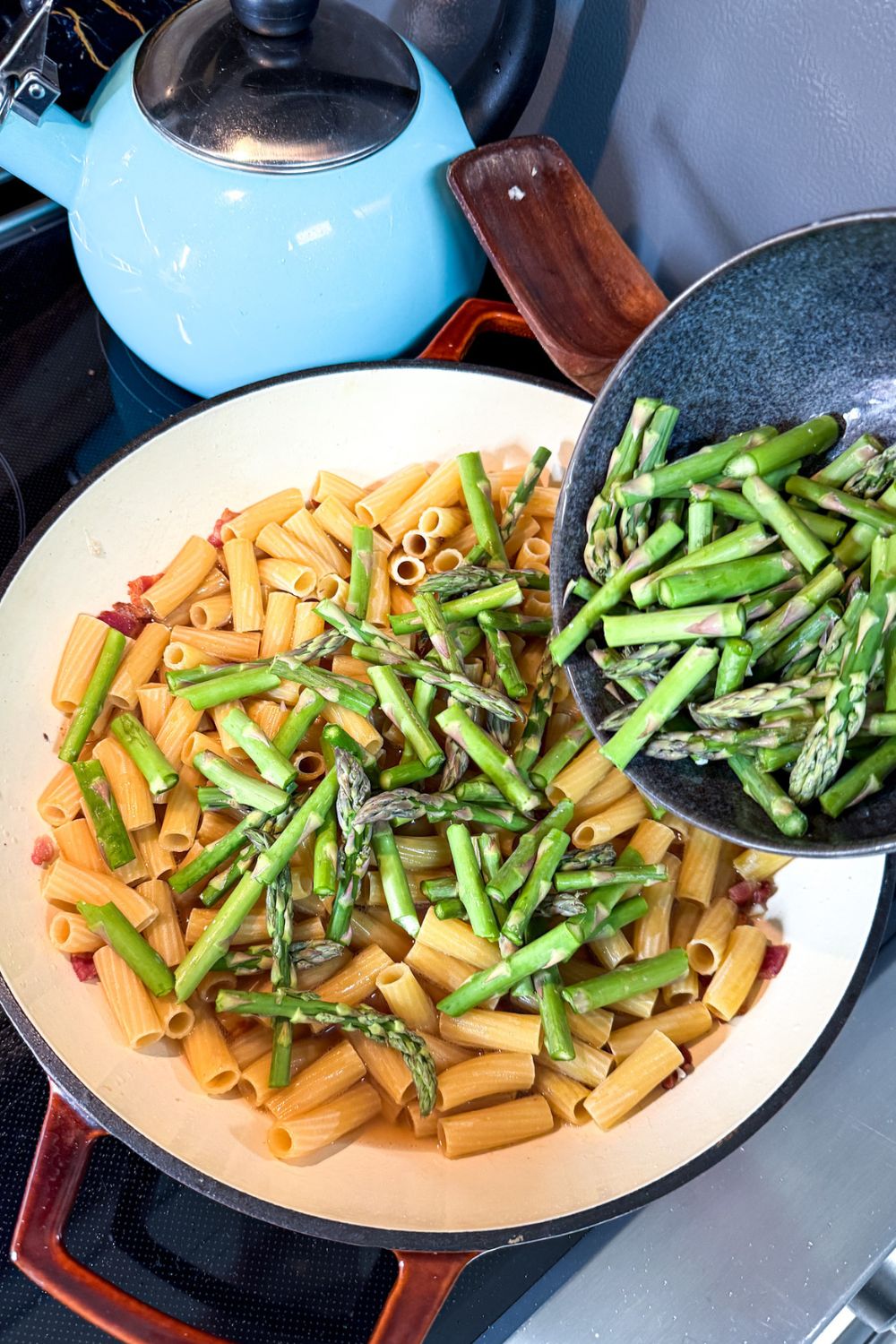 Rigatoni pasta and asparagus cooking together in broth in one pot