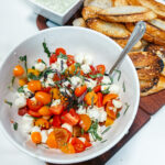 marinated cherry tomato mozzarella salad surrounded by crostinis on a cutting board.