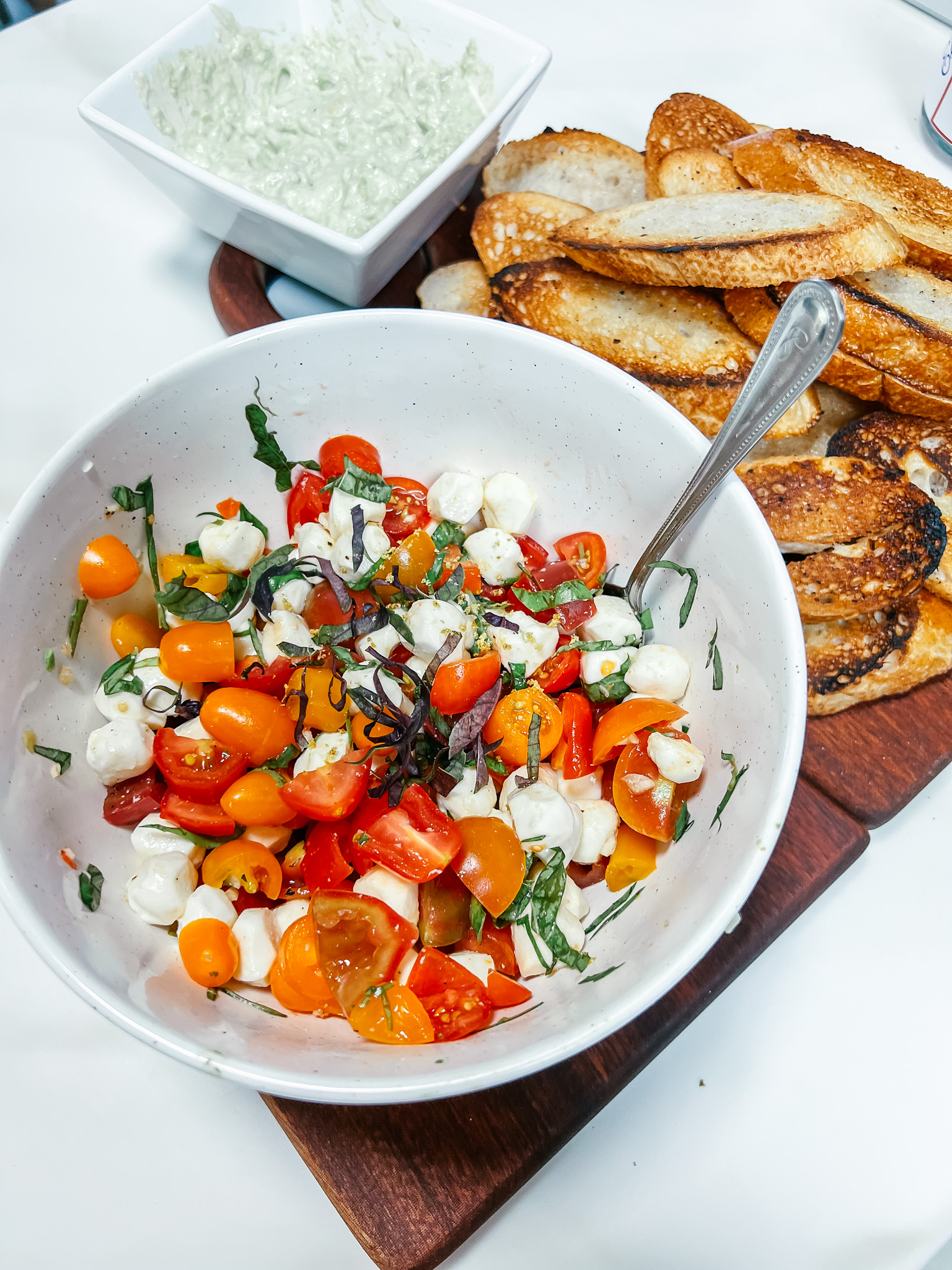 marinated cherry tomato mozzarella salad surrounded by crostinis on a cutting board.