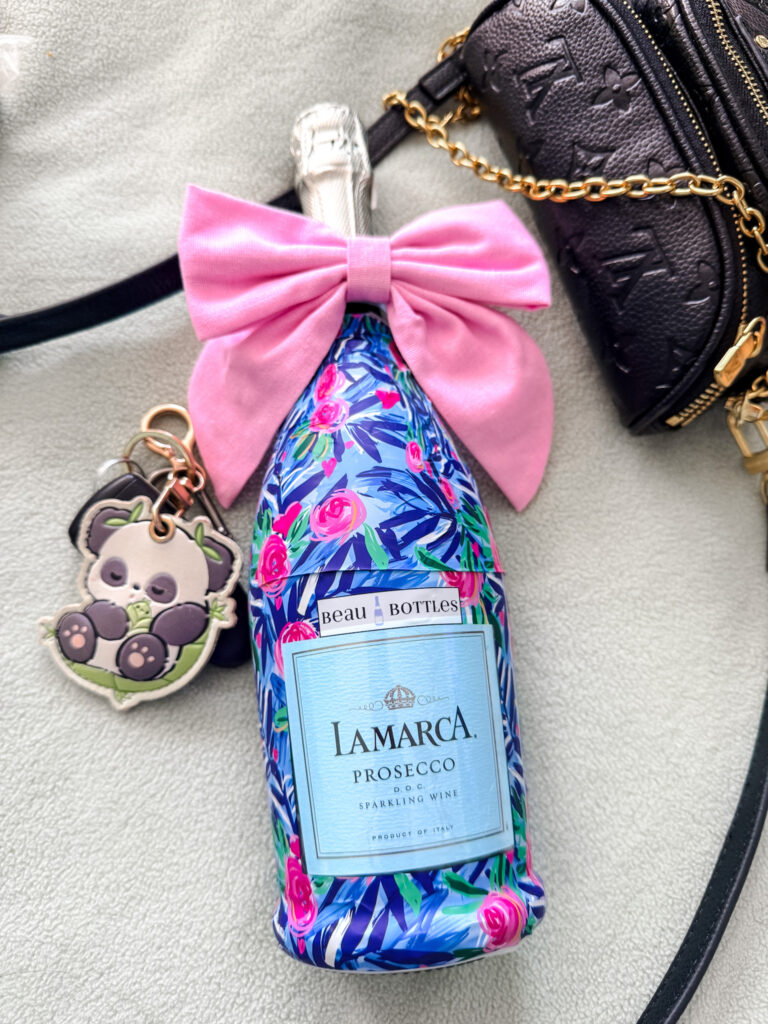 Decorative champagne bottle wrap with pink bow on a prosecco bottle styled with purse and keys as a hostess gift idea