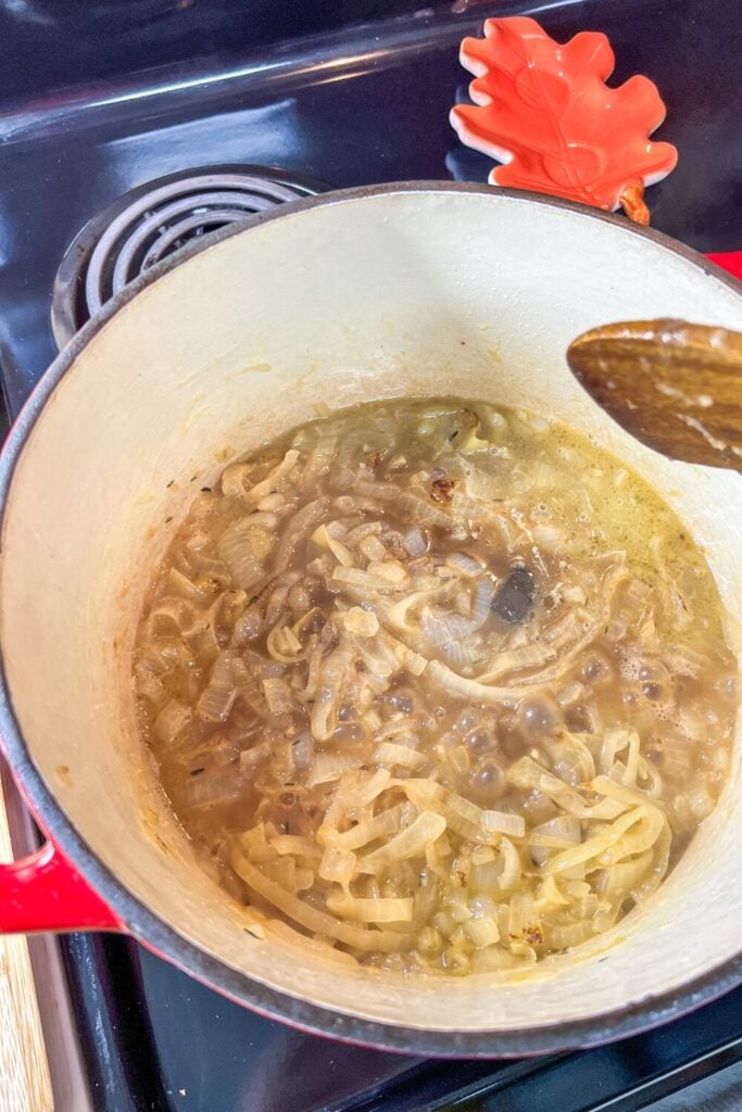 cooked sliced onions, chopped garlic, and thyme, in a cast iron pot on the stove Cooking down