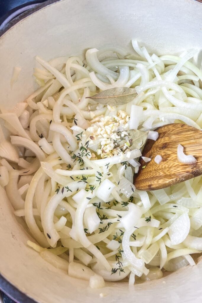 sliced onions, chopped garlic, and thyme, in a cast iron pot on the stove