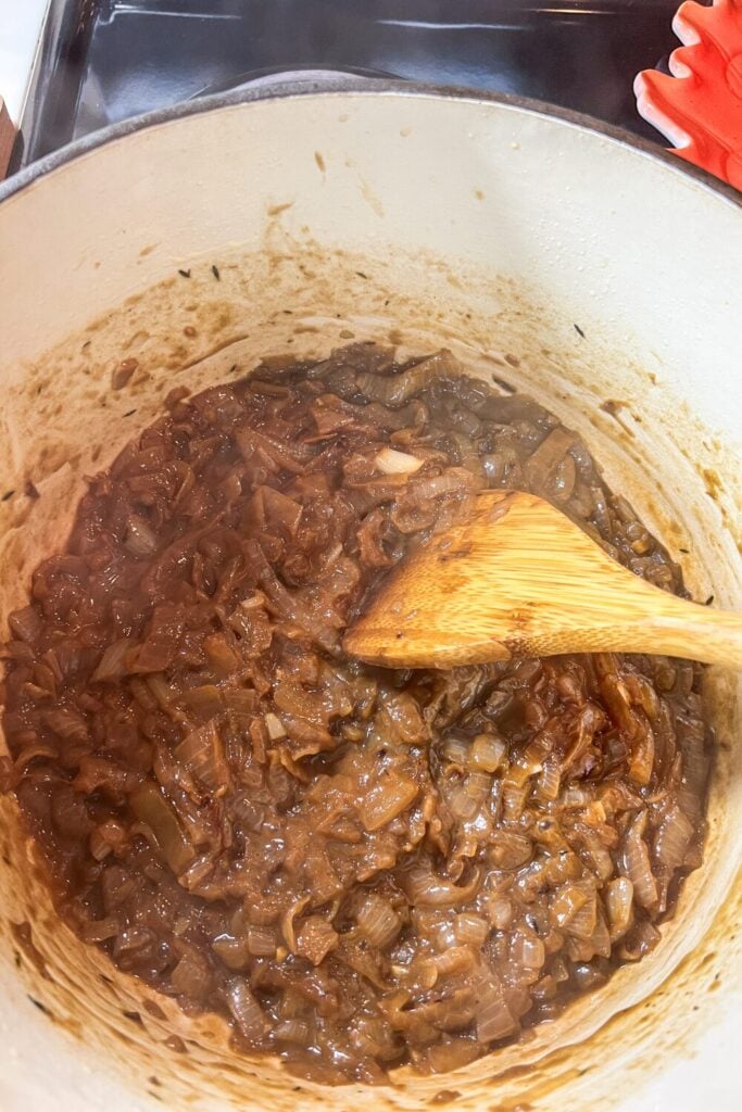 cooked sliced onions, chopped garlic, and thyme, in a cast iron pot on the stove ready for beef broth