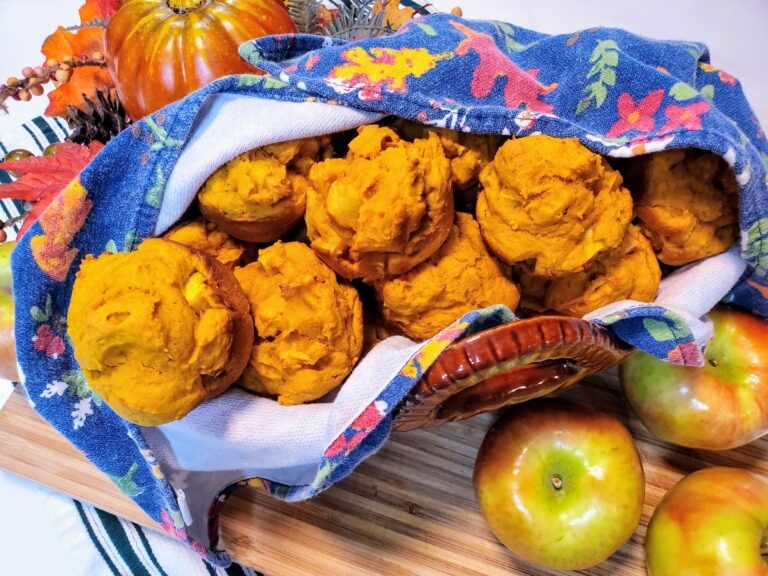 Small apple pumpkin muffins in a color lined basket next to a fake pumpkin.