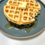 finished waffle with a pad of butter and syrup on a dark ceramic plate