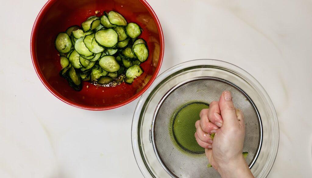 Squeezing the last of the cucumbers the rest are in the bowl with the dressing.