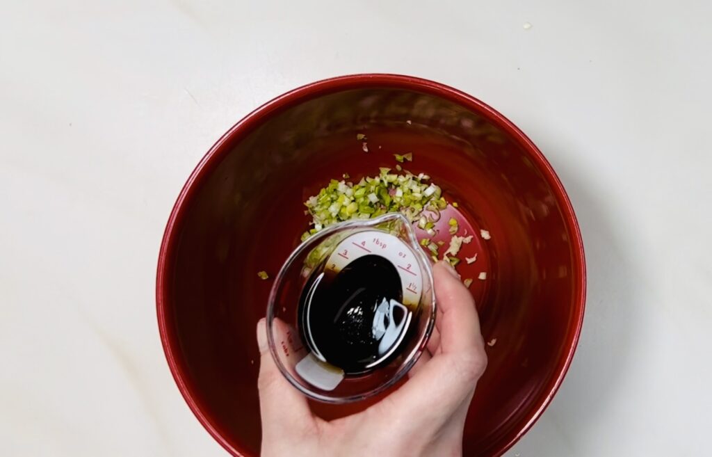 the liquids in a measuring cup and the green onion and garlic in the bowl.