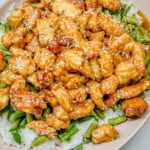 Orange Sesame Chicken on top of green beans and white rice in an oval platter.