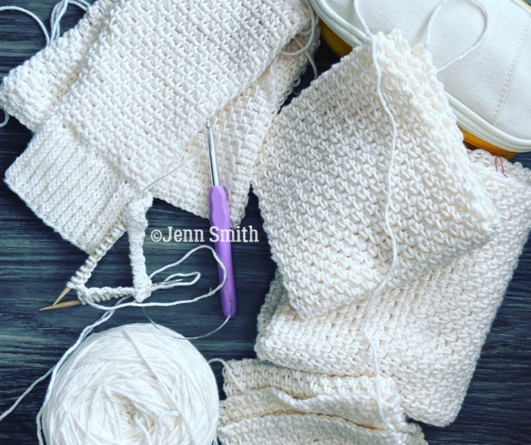 image of the completed panels, crochet hook, and the start of the sleeves on the knitting needles.