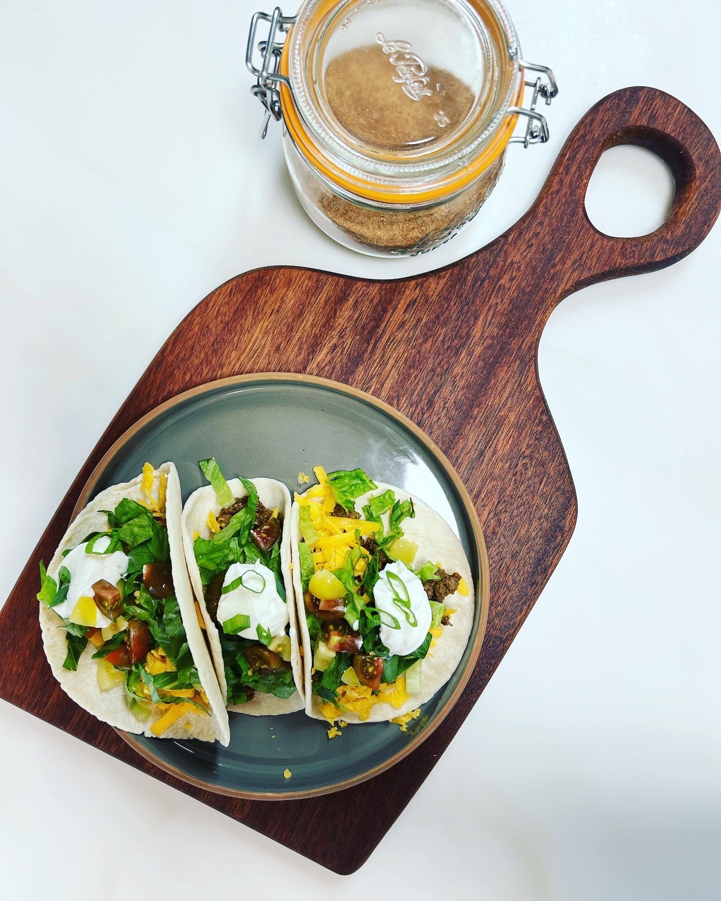 Tacos on a cutting board with a jar of the taco seasoning on it.