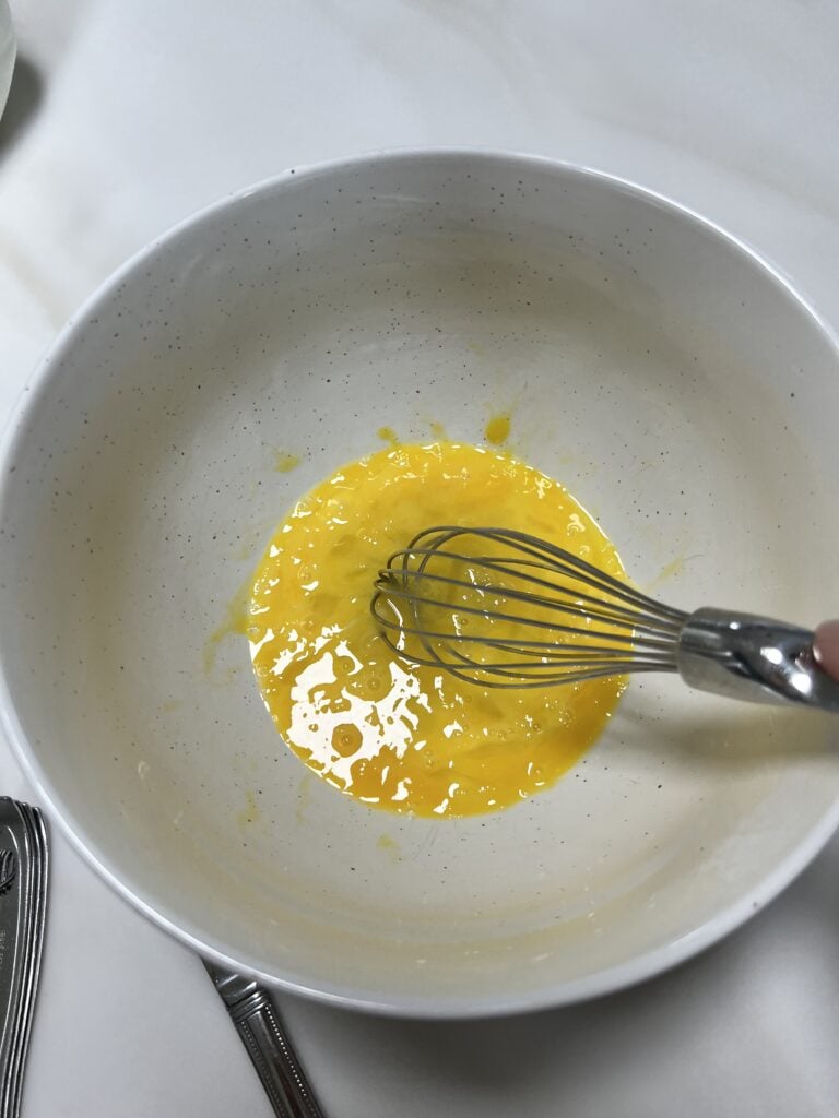 Eggs with a whisk in a bowl broken up a bit