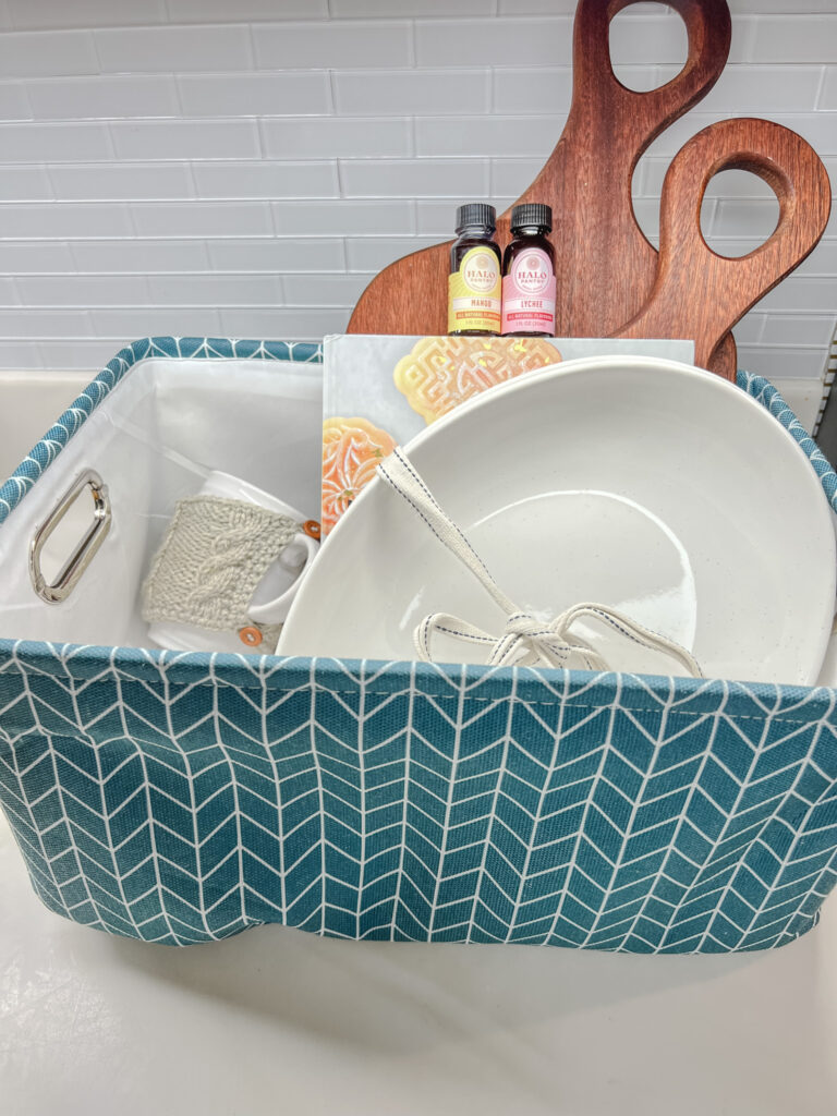 A soft style storage bin with a cup wrapped with a cup sweater, the cuddle boards, Modern Asian Cookbook, mora ceramic platters, and Halo Pantry flavors.