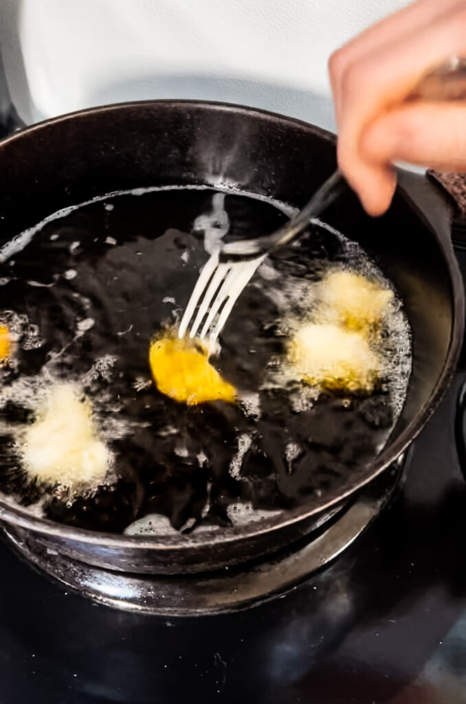 Close of the chicken being dropped into the fryer oil.