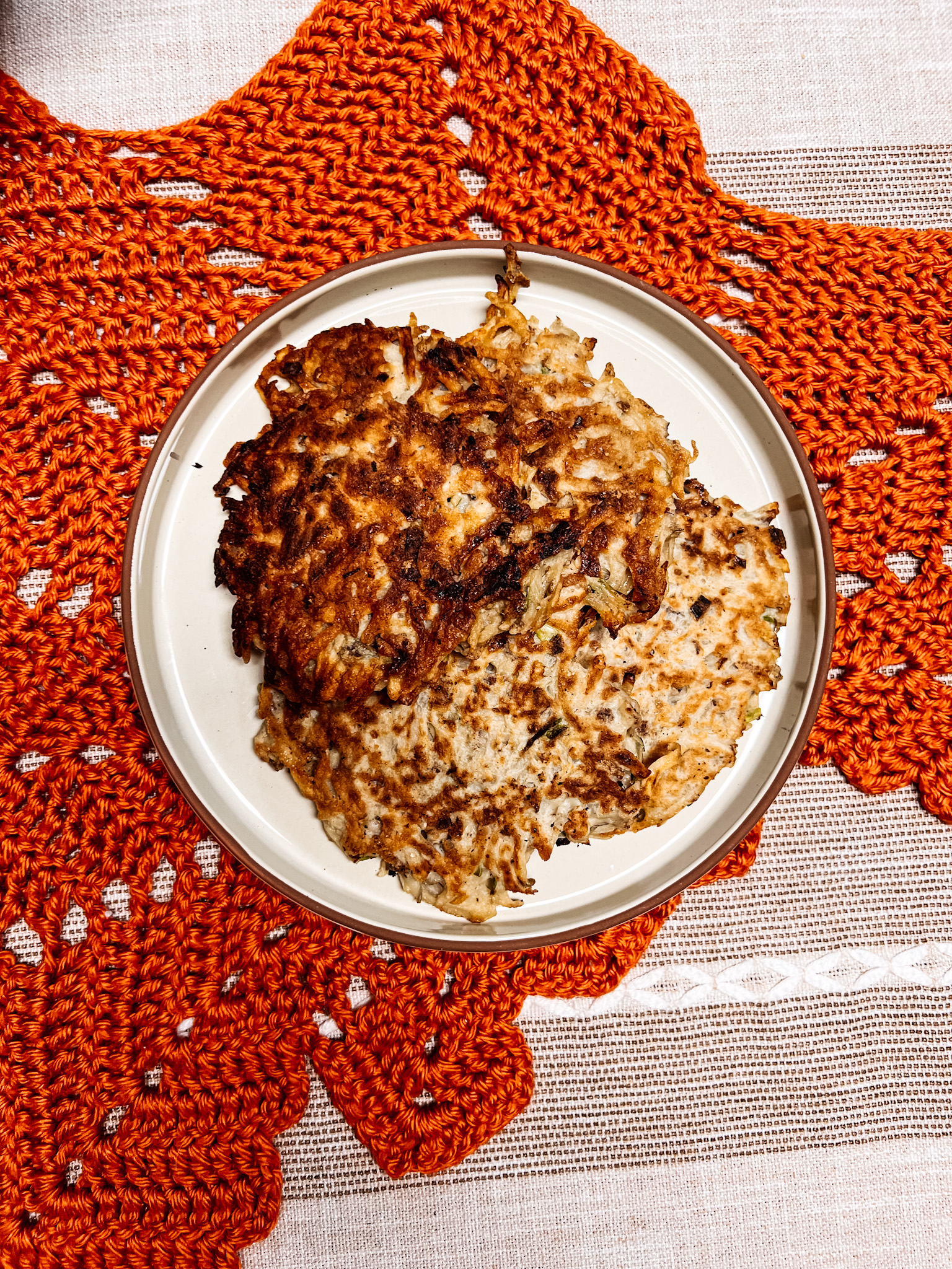 scallion potato pancakes on a ceramic plate sitting on a crocheted runner.