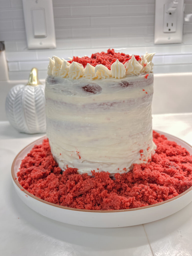 Finished Red Velvet Cake sitting on a ceramic plate surrounded by red velvet crumble.