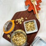 Pumpkin seeds in a jar and small bowl with a spoon and leaf plate.