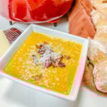 Butternut squash soup in a square bowl topped with bacon and Parmesan cheese