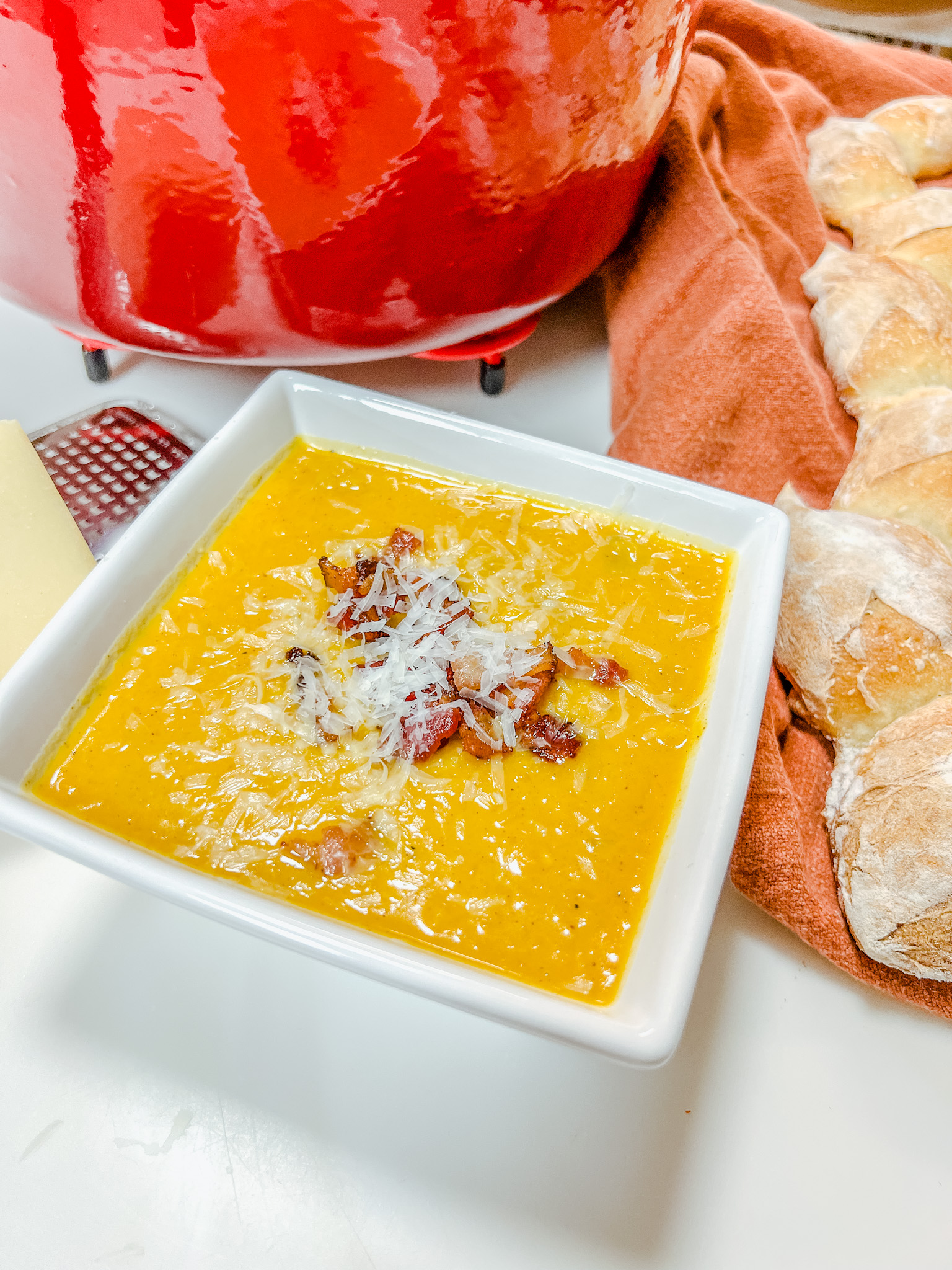 Butternut squash soup in a square bowl topped with bacon and Parmesan cheese