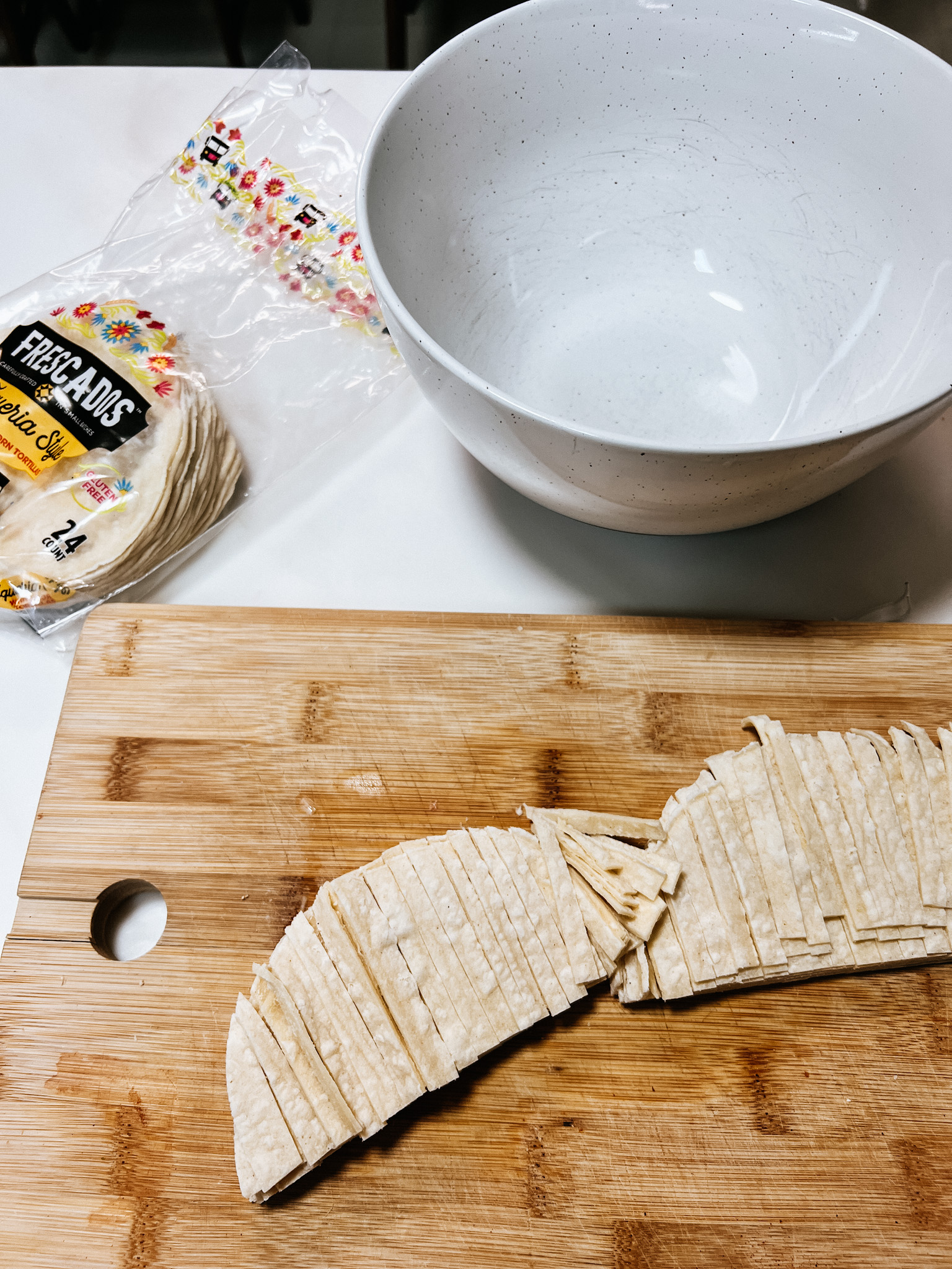 a mixing bowl next to corn tortillas cut into strips on a bamboo cutting board.