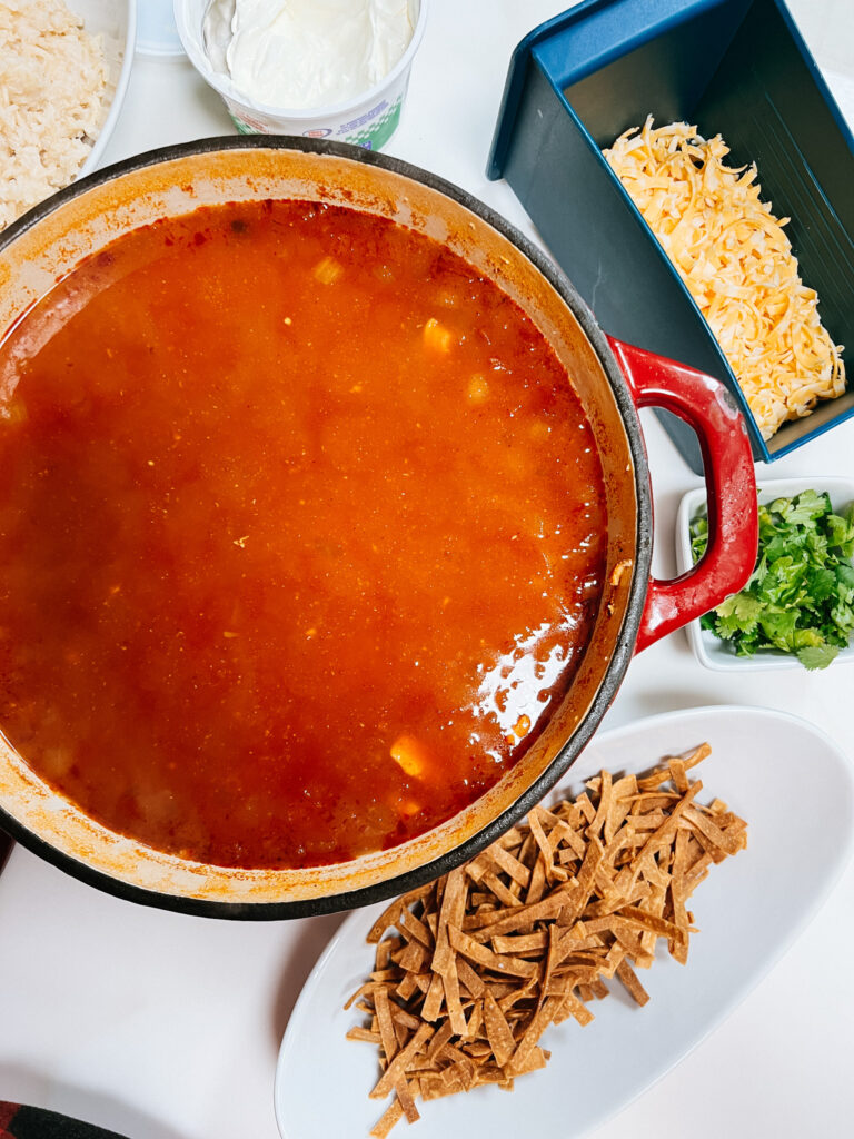 Tortilla soup in a large cast iron pot surrounded by the toppings to put on the soup.