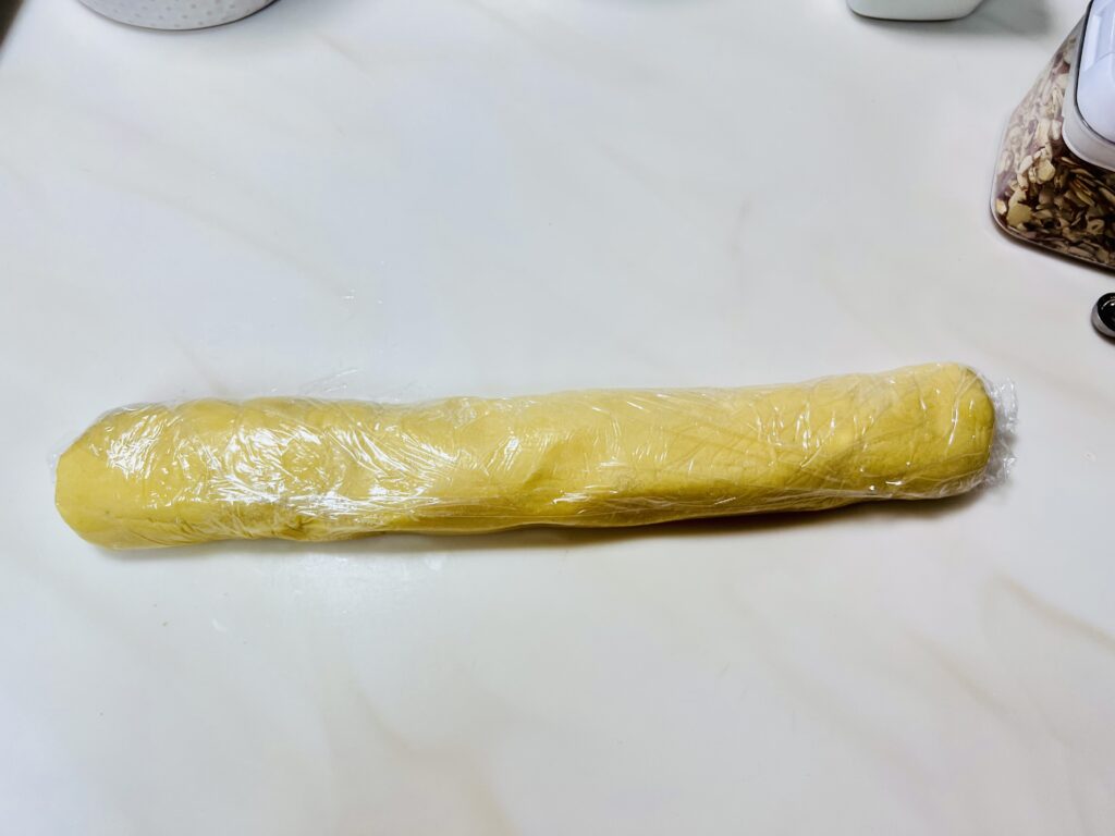 Chinese almond cookie dough wrapped up in a log shape in cling wrap.