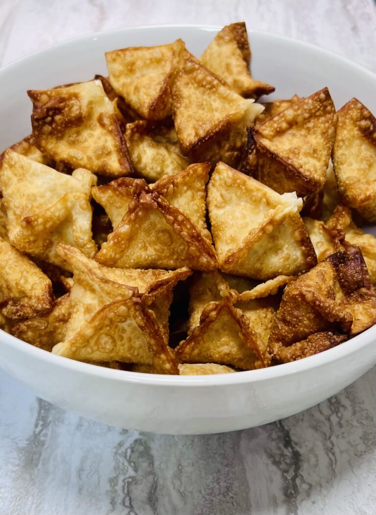 Finished crab rangoon (cream cheese wontons) in the square-gift shape, in a white bowl.