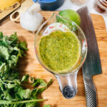 cilantro marinade finished in a measuring cup laying on a cutting board, surrounded by the ingredients