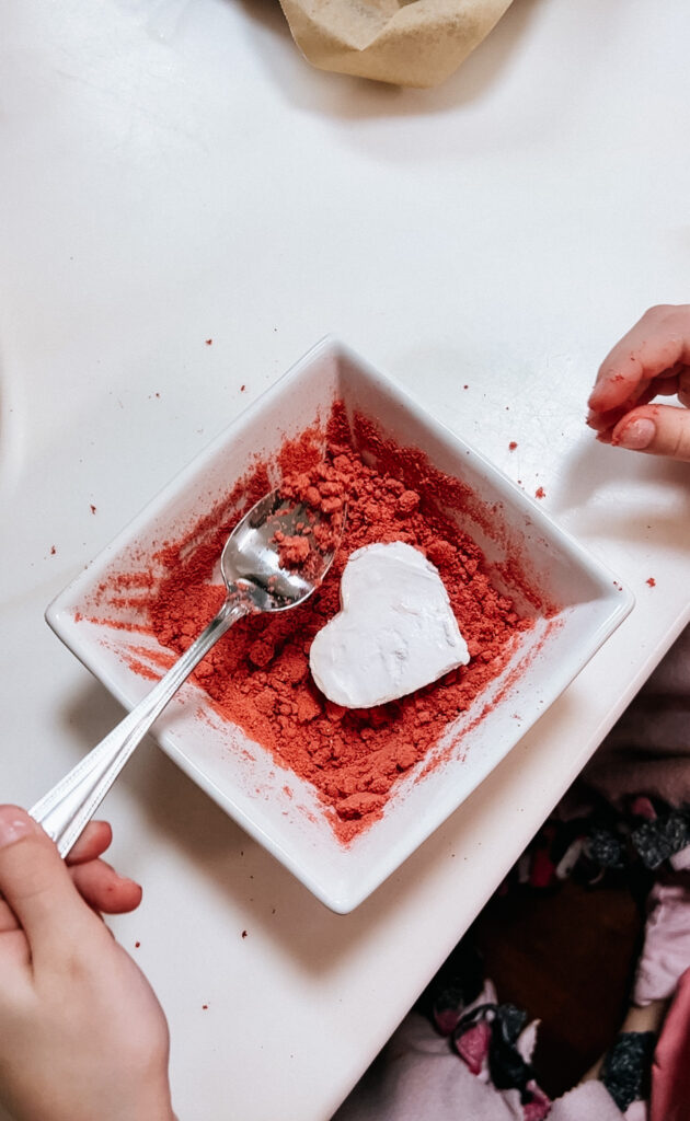 A spoon being used to cover the marshmallow in the strawberry powder.