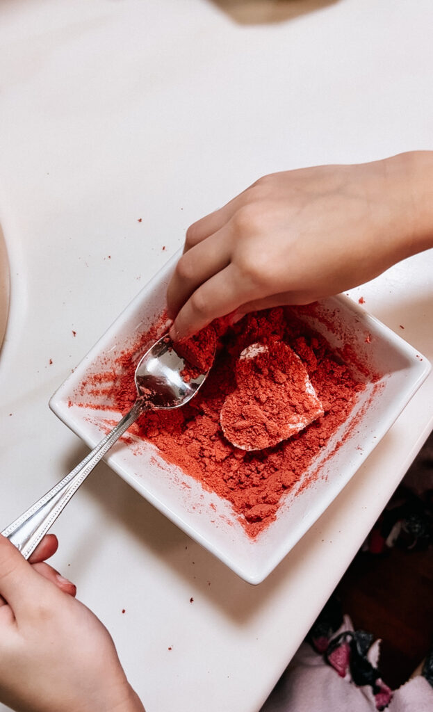 A spoon being used to continue covering the marshmallow in the strawberry powder.