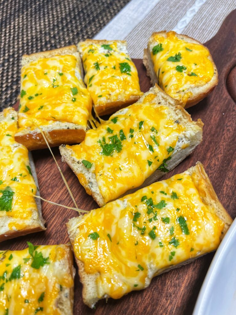Image of the cheesy garlic bread sliced into pieces, close up. The bread slices are on a wood cutting board.