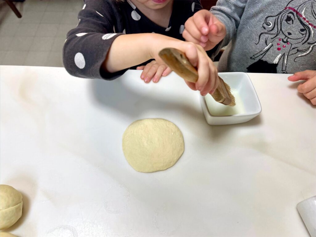child brushing oil onto bao dough before folding for steamed bao buns