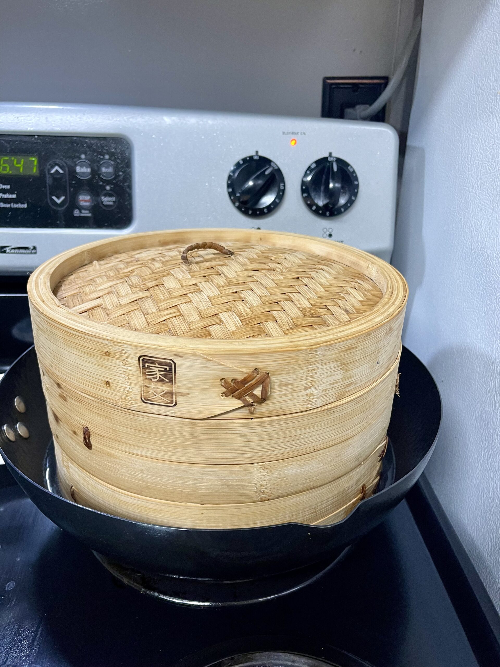 bamboo steamer stacked on a wok steaming bao buns on the stovetop